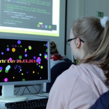 A girl, sitting infront of a computer screen, is coding her individual screen saver.